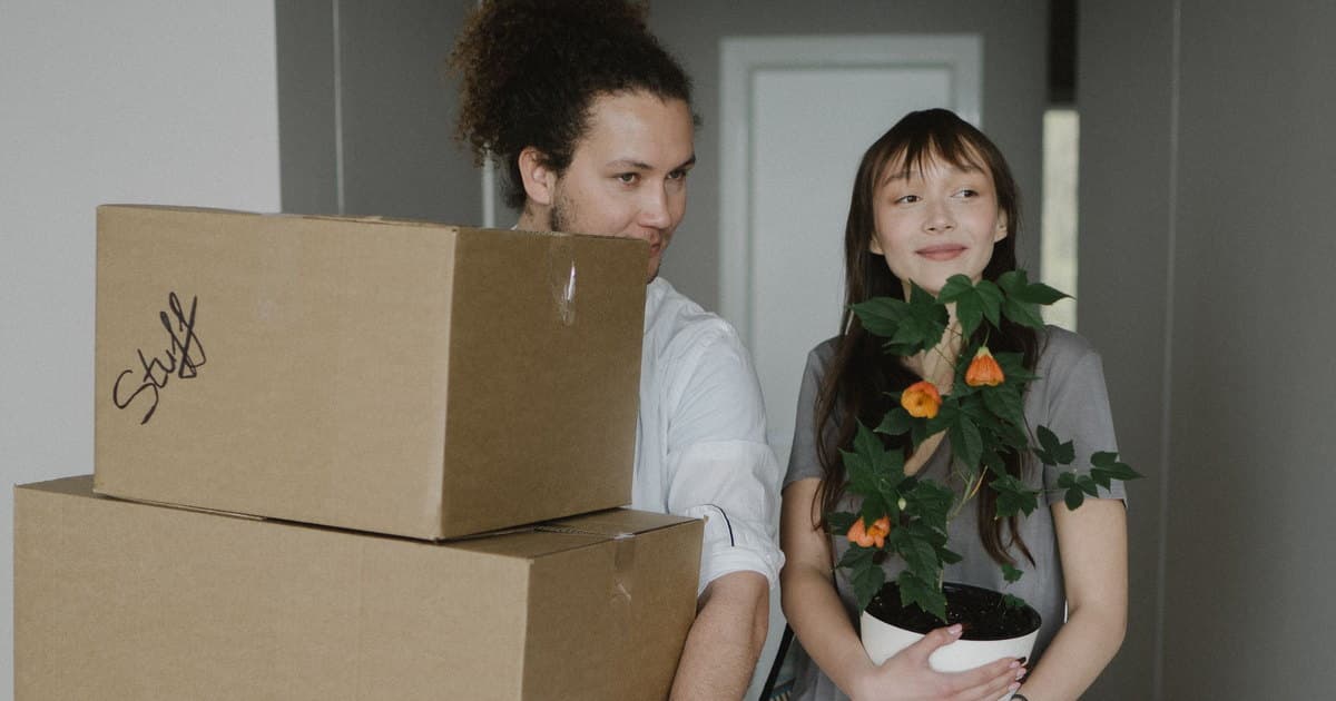 Dos jóvenes cargan cajas y una planta el día de la mudanza a su piso nuevo