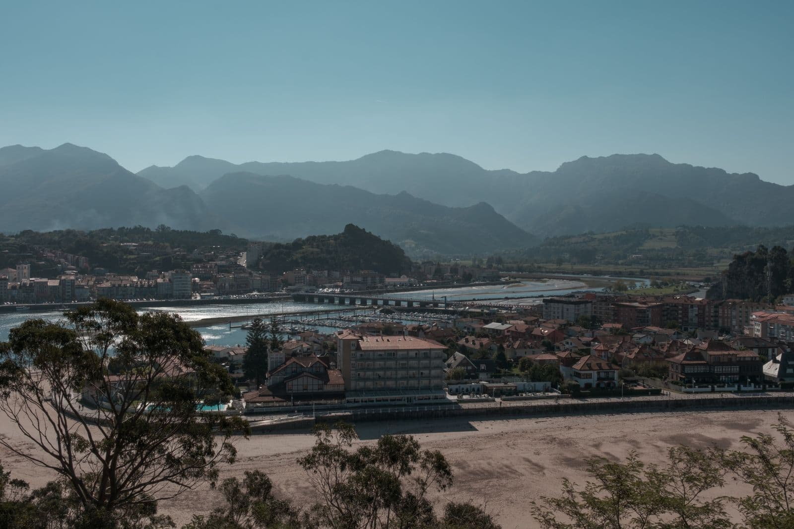 Villa costera asturiana con viviendas junto a la ría, puerto deportivo y montañas al fondo