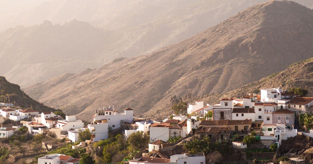Casas blancas de un pueblo canario escalonadas en la ladera de un barranco, con las montañas de la isla al fondo