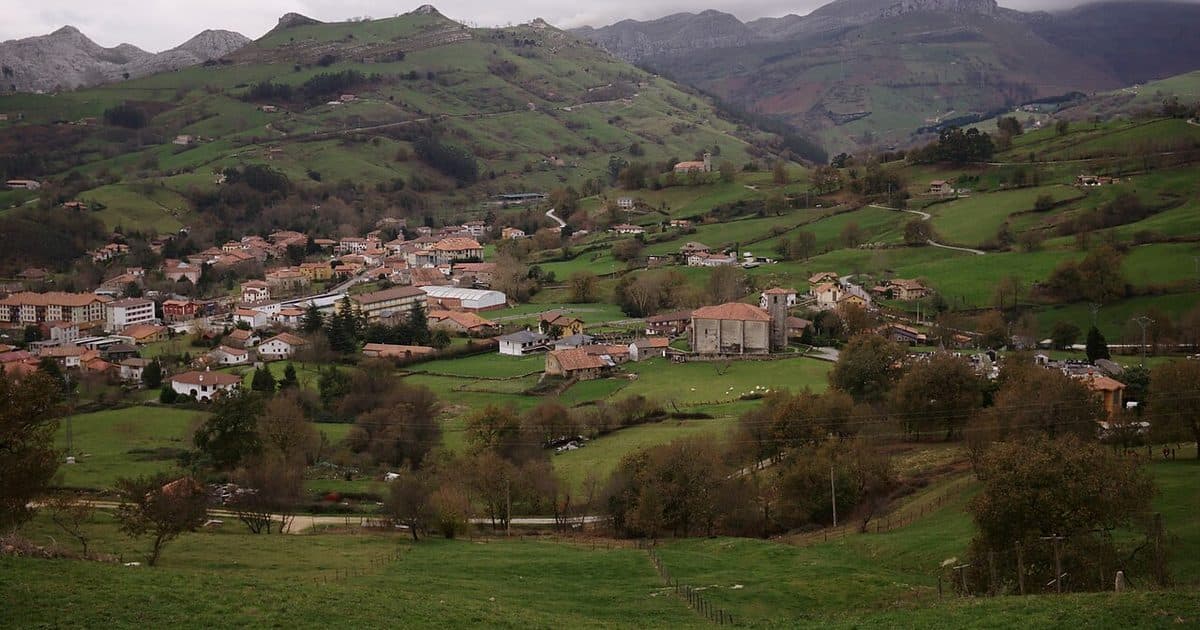 Pueblo cántabro de casas con tejado de teja roja e iglesia, con prados verdes y montañas al fondo