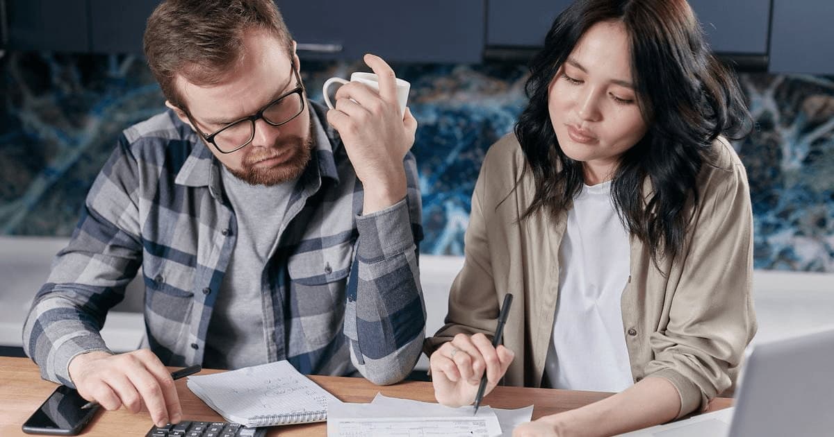 Una pareja hace cuentas con calculadora y papeles en la mesa de la cocina