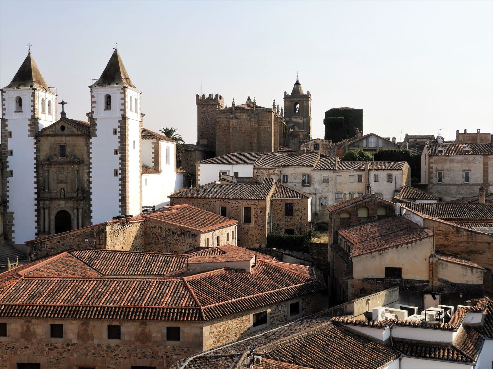 Tejados de casas de piedra del casco antiguo de Cáceres con torres de iglesia y una torre de castillo al fondo