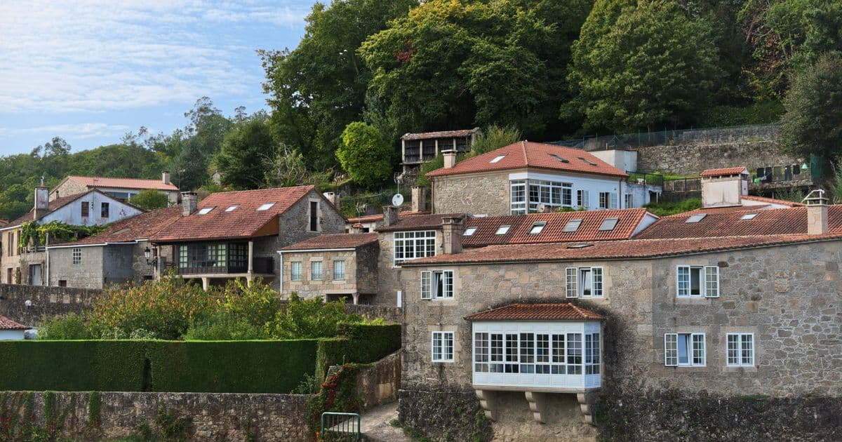 Casas gallegas de piedra con galerías acristaladas y tejados de teja, escalonadas entre vegetación en una aldea